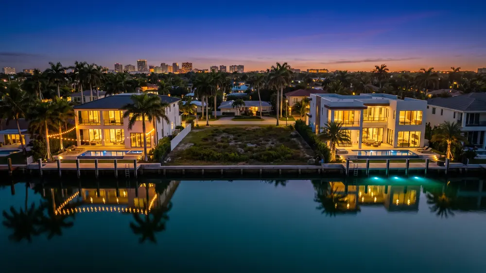 A vacant lot at dusk between two lit modern homes.
