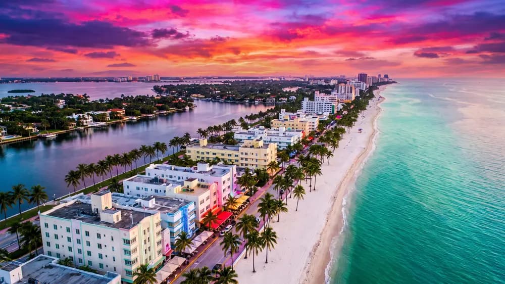 Miami Beach from above at sunset under a magenta sky, the ocean on one side and the bay on the other.