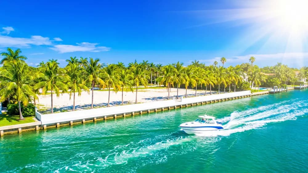 A vacant canal lot under midday sun, turquoise water and a speedboat wake.